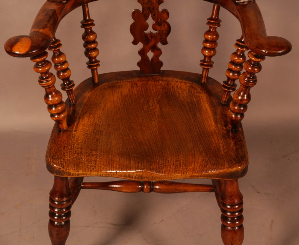 An antique brown yew wood Windsor armchair featuring a hoop back, a central pierced splat, turned spindles, broad armrests, and turned legs. View V