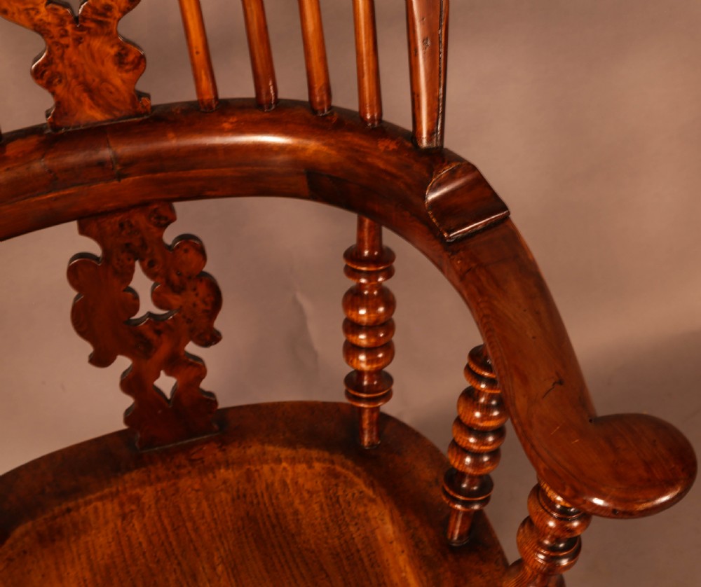 An antique brown yew wood Windsor armchair featuring a hoop back, a central pierced splat, turned spindles, broad armrests, and turned legs. View X