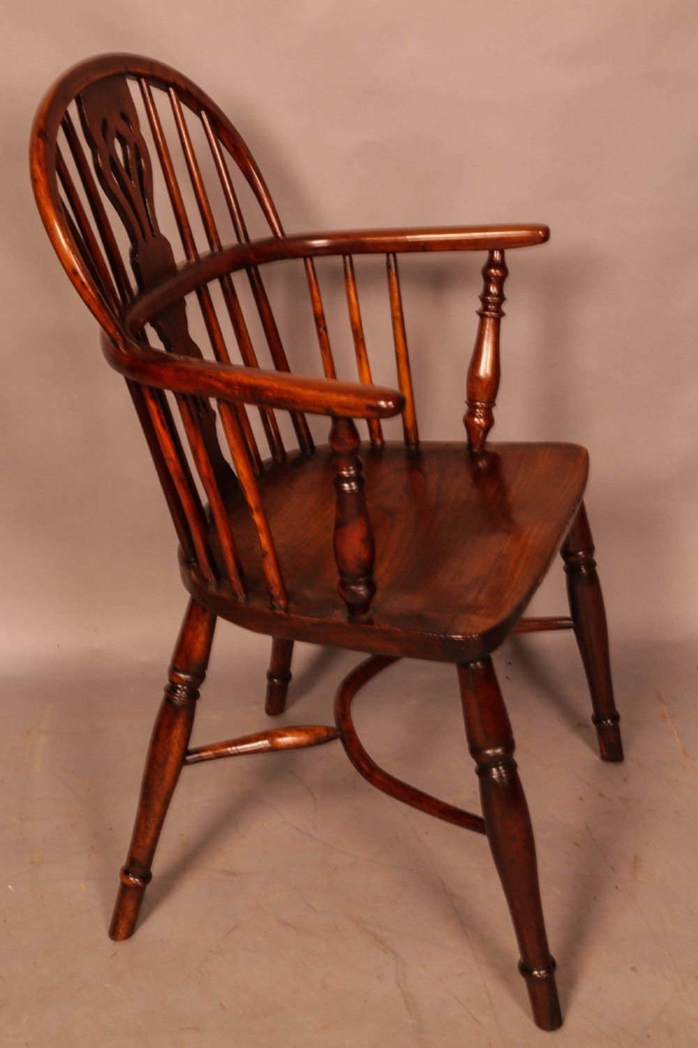 A yew wood low-back Windsor armchair featuring a curved top rail, pierced back splat, spindled arms, shaped solid seat, turned legs, and a crinoline stretcher.