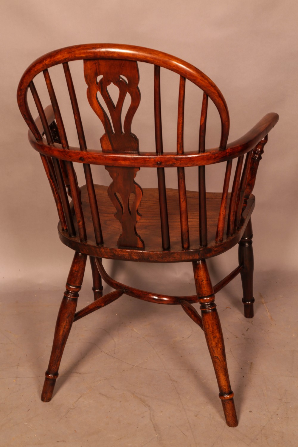 A yew wood low-back Windsor armchair featuring a curved top rail, pierced back splat, spindled arms, shaped solid seat, turned legs, and a crinoline stretcher. View III