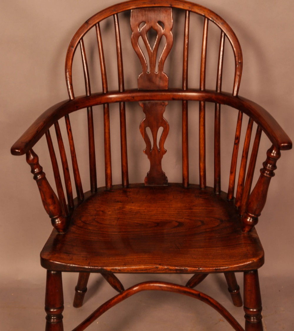 A yew wood low-back Windsor armchair featuring a curved top rail, pierced back splat, spindled arms, shaped solid seat, turned legs, and a crinoline stretcher. View IV