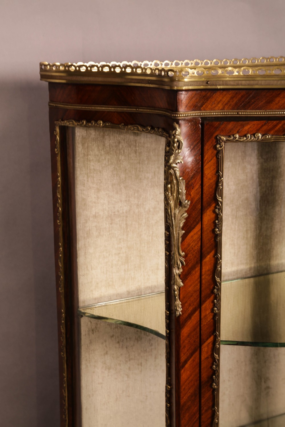 An upright curved glass display cabinet veneered in rich brown kingwood with intricate cast ormolu mounts and glass shelving. View V