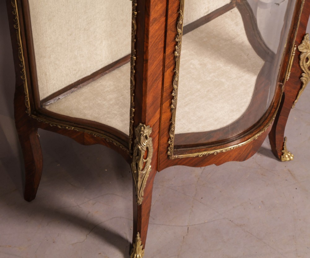 An upright curved glass display cabinet veneered in rich brown kingwood with intricate cast ormolu mounts and glass shelving. View VIII