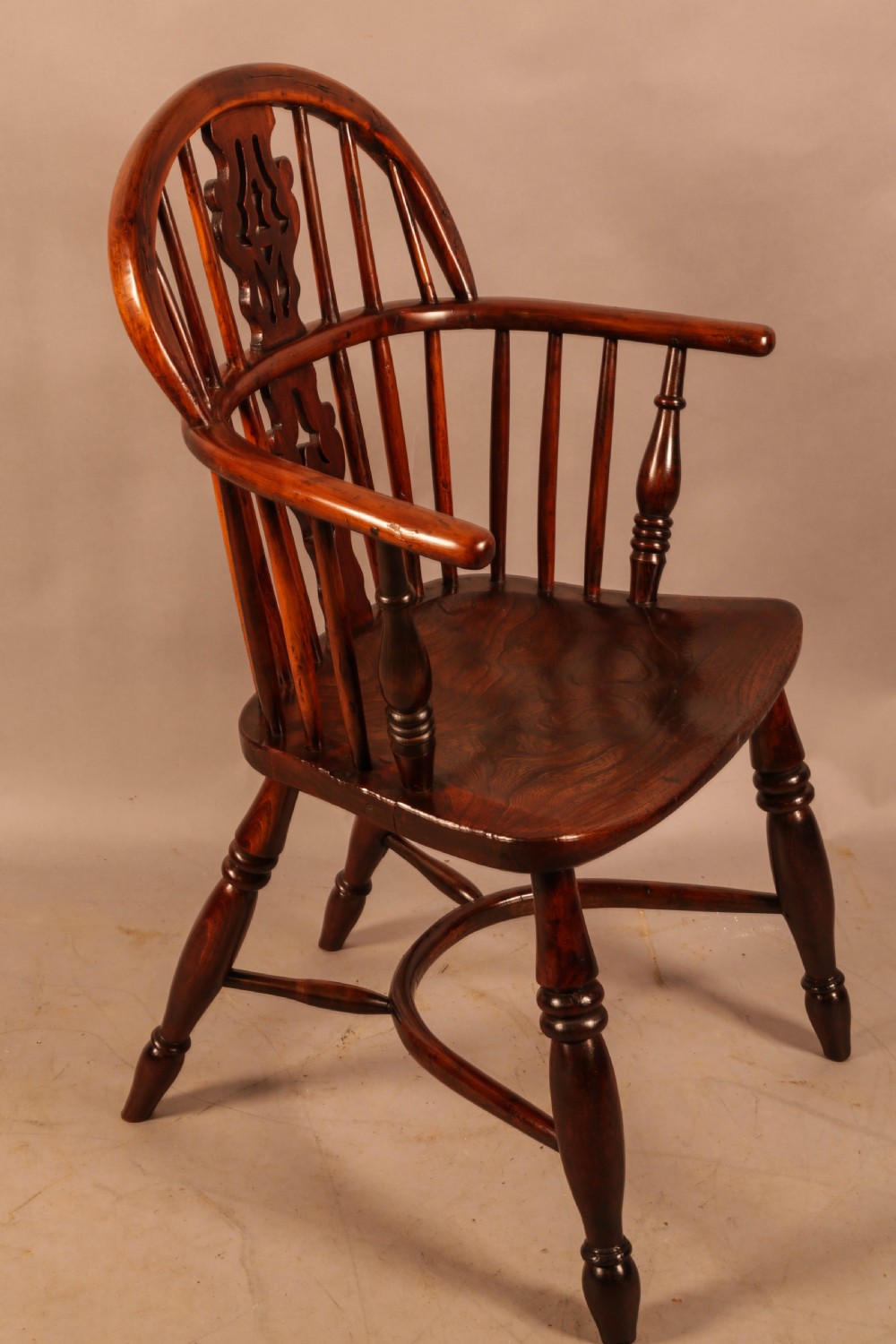 A nineteenth-century yew wood Windsor armchair featuring a curved hoop back, pierced central splat, turned arm supports, shaped saddle seat, and turned legs with a crinoline stretcher.