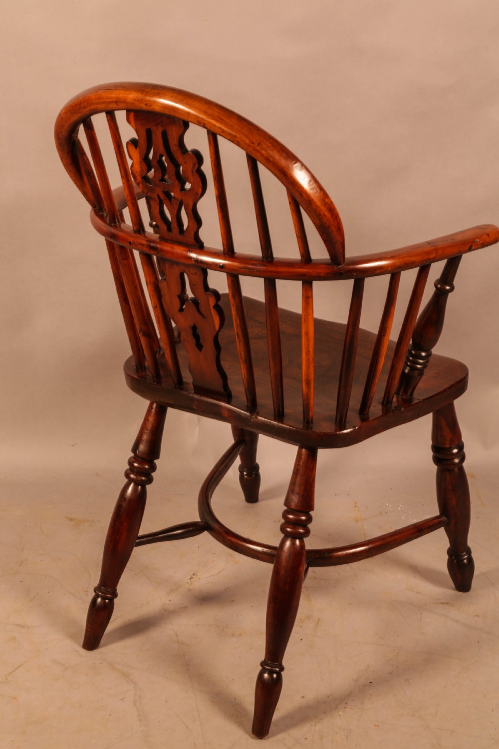 A nineteenth-century yew wood Windsor armchair featuring a curved hoop back, pierced central splat, turned arm supports, shaped saddle seat, and turned legs with a crinoline stretcher. View V