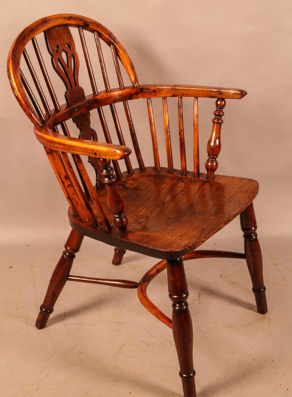 An antique yew wood low-back Windsor armchair featuring turned legs, a crinoline stretcher, and a pierced splat.
