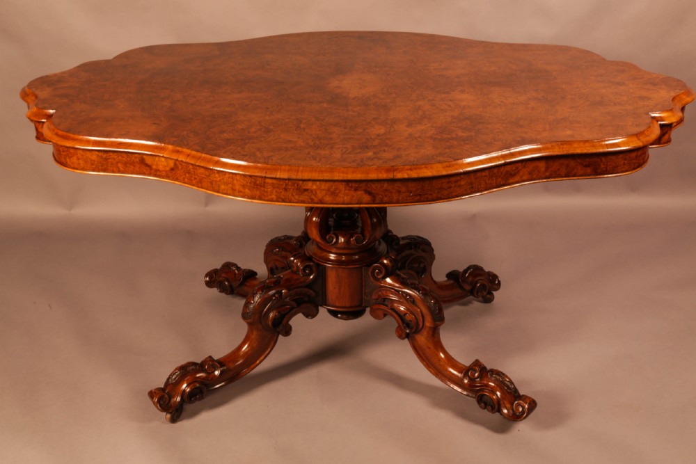 A Victorian burr walnut breakfast table featuring a shaped serpentine top resting on a central carved pedestal column with four scroll-carved legs.