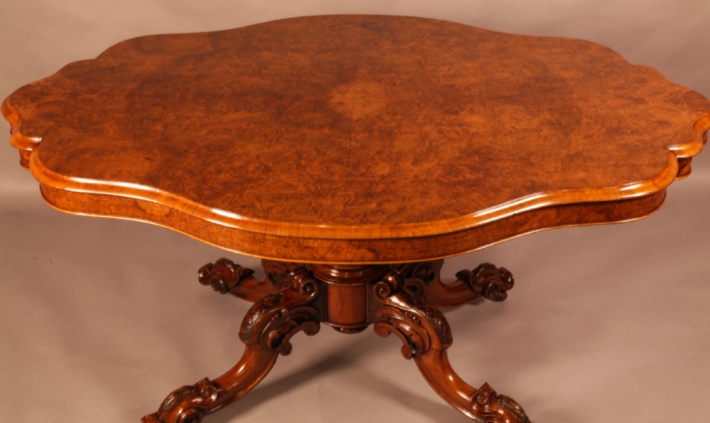 A Victorian burr walnut breakfast table featuring a shaped serpentine top resting on a central carved pedestal column with four scroll-carved legs. View IV
