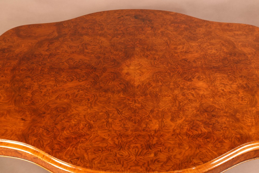 A Victorian burr walnut breakfast table featuring a shaped serpentine top resting on a central carved pedestal column with four scroll-carved legs. View V