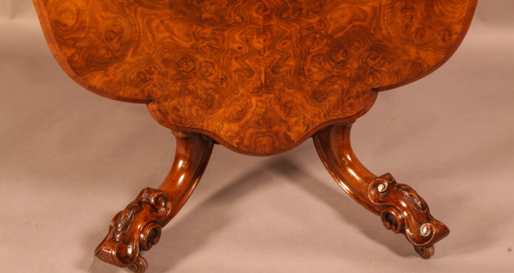 A Victorian burr walnut breakfast table featuring a shaped serpentine top resting on a central carved pedestal column with four scroll-carved legs. View VI