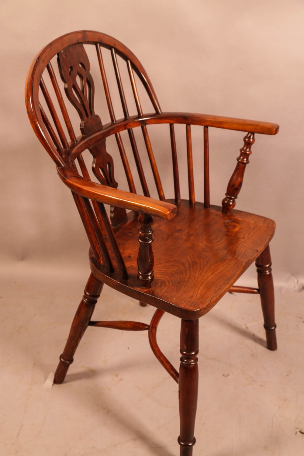 A low-back yew wood Windsor armchair featuring turned legs, a shaped seat, a pierced central back splat, and a curved crinoline stretcher.