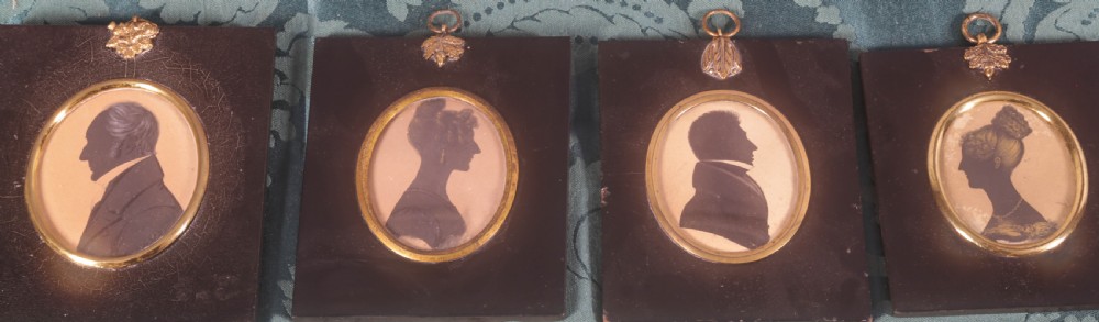 Four framed antique silhouette profile portraits in rectangular papier-mache frames with oval brass bezels and decorative metal hangers. View II