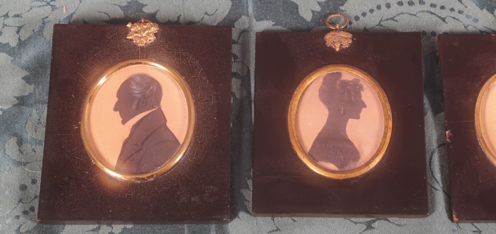 Four framed antique silhouette profile portraits in rectangular papier-mache frames with oval brass bezels and decorative metal hangers. View III