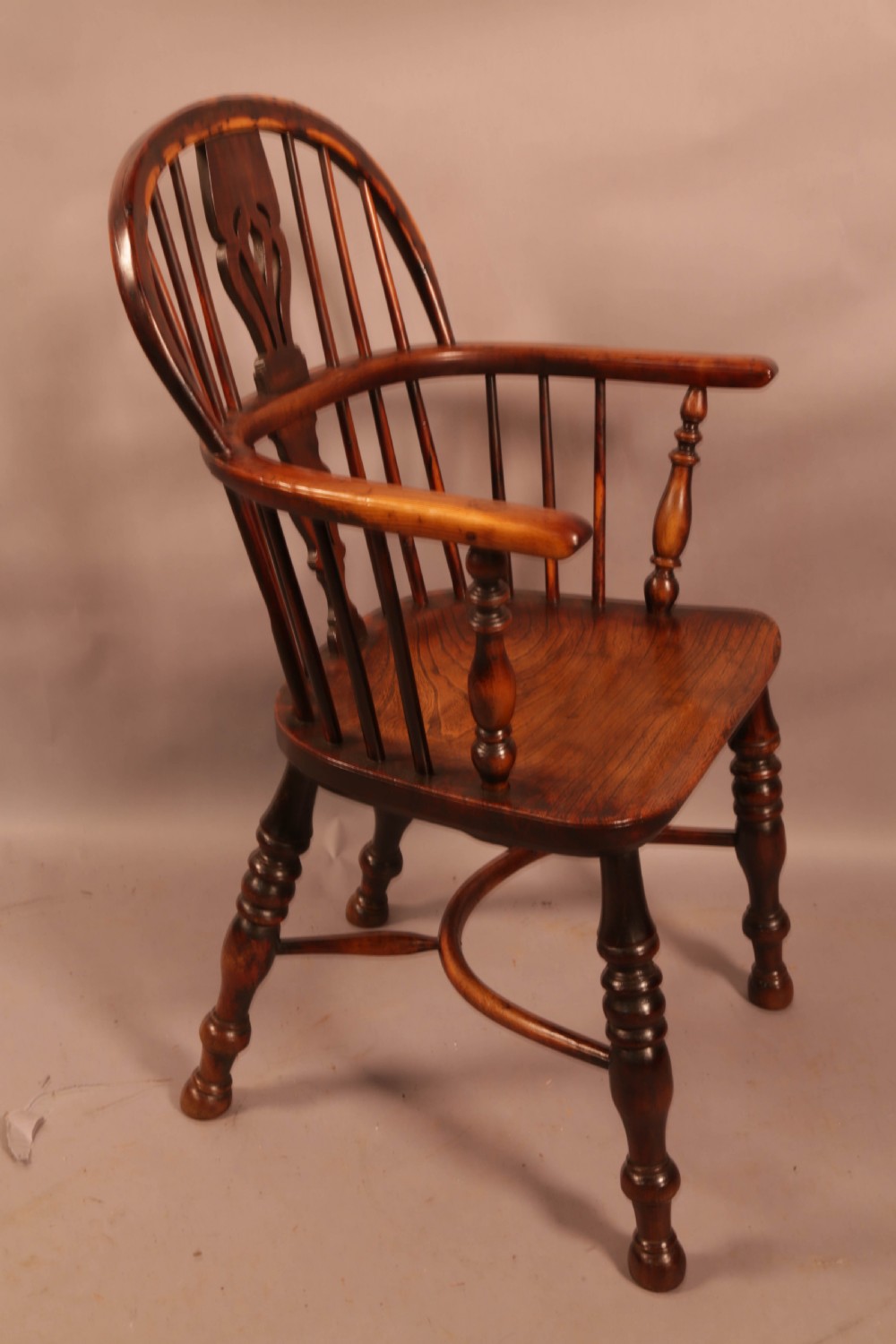 An antique yew wood Windsor armchair with a hoop back, pierced splat, curved armbow, turned legs, and a crinoline stretcher.