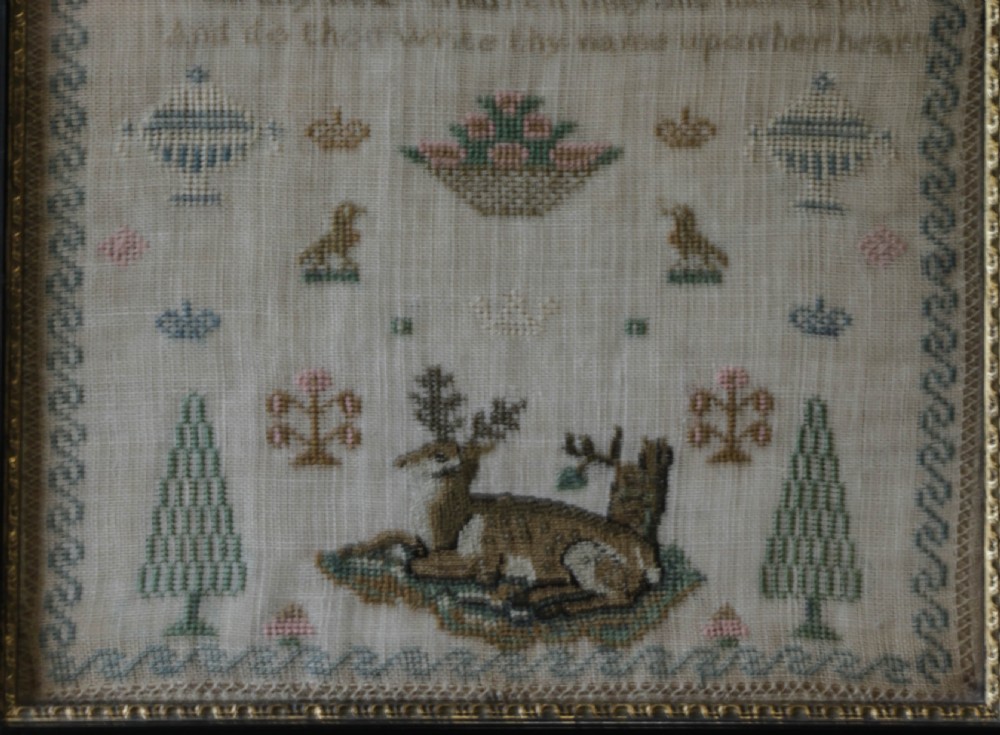 A framed 19th-century needlework sampler on linen featuring embroidered alphabets, numbers, a central verse, floral borders, and a reclining stag motif. View VII