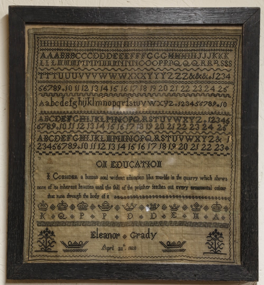 A framed 1820 Georgian needlework sampler featuring embroidered alphabets, numbers, crowns, and a central verse titled On Education on a linen ground.