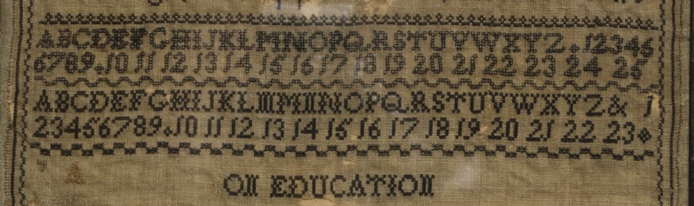 A framed 1820 Georgian needlework sampler featuring embroidered alphabets, numbers, crowns, and a central verse titled On Education on a linen ground. View IV
