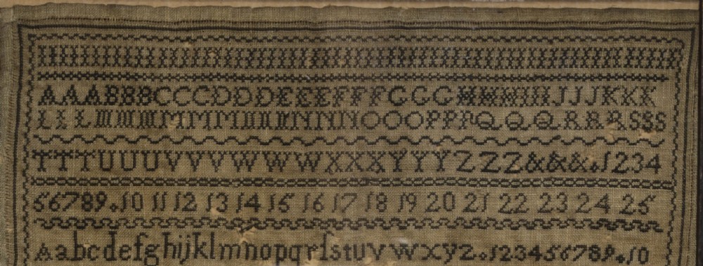 A framed 1820 Georgian needlework sampler featuring embroidered alphabets, numbers, crowns, and a central verse titled On Education on a linen ground. View V