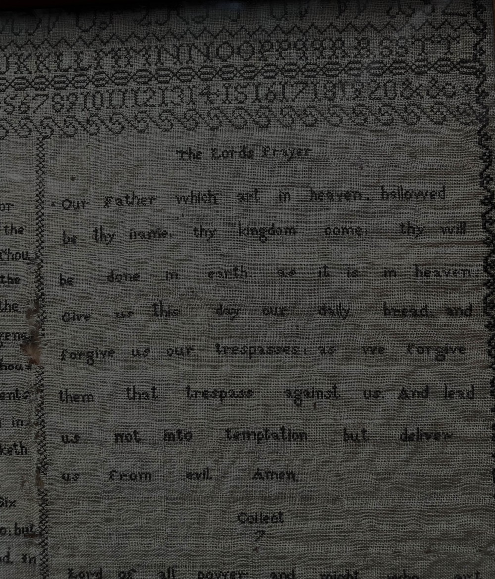 An 1827 Georgian embroidered needlework sampler featuring the Ten Commandments, the Lords Prayer, and an alphabet border set in a wooden frame. View V
