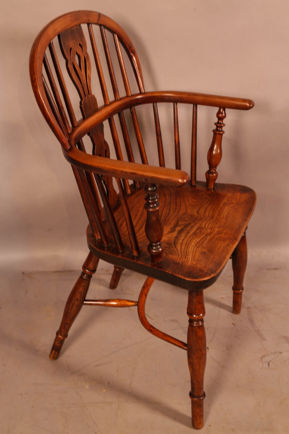 An antique yew wood low back Windsor armchair featuring a pierced central splat, steam-bent arm rail, turned legs, and a crinoline stretcher.