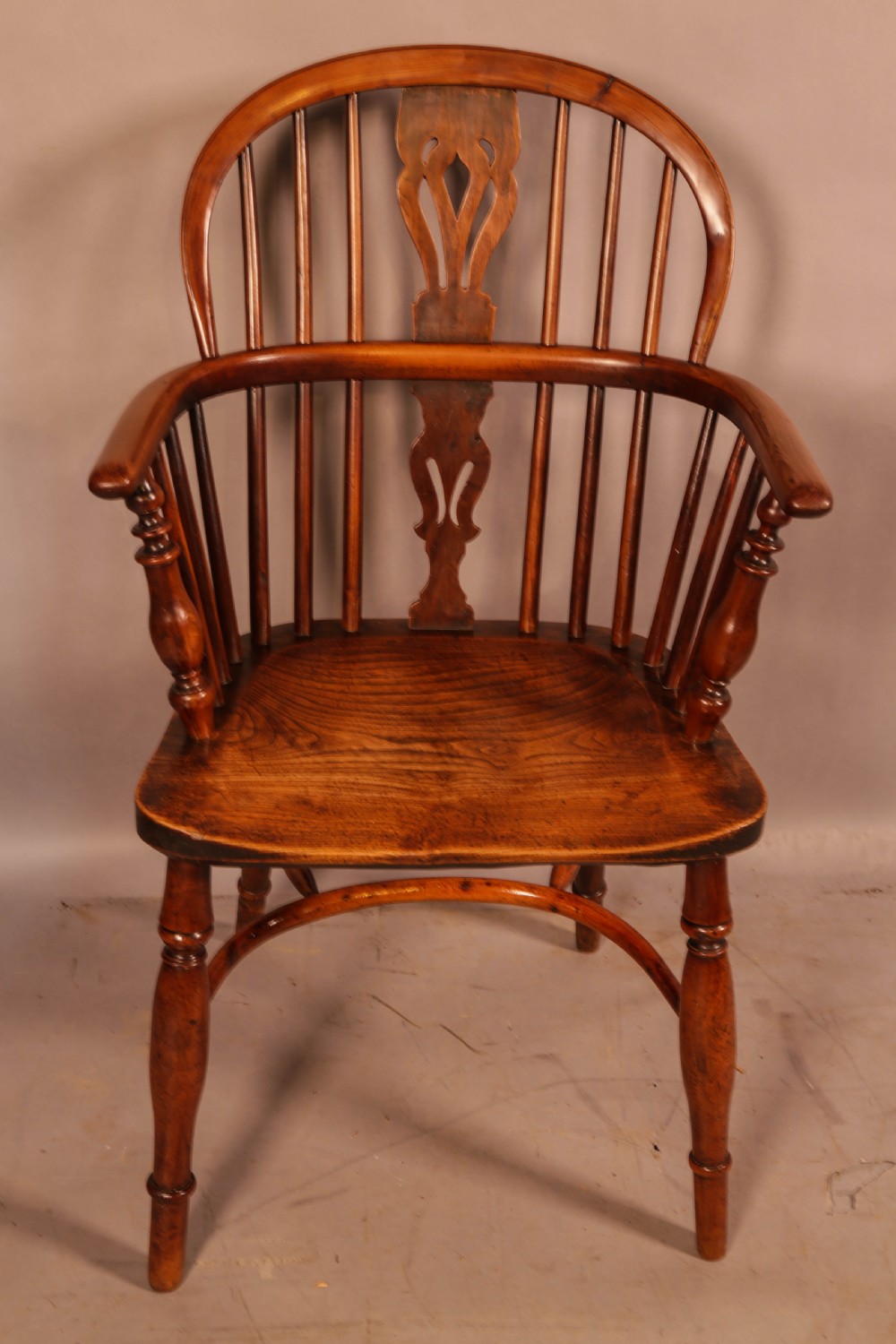 An antique yew wood low back Windsor armchair featuring a pierced central splat, steam-bent arm rail, turned legs, and a crinoline stretcher. View II