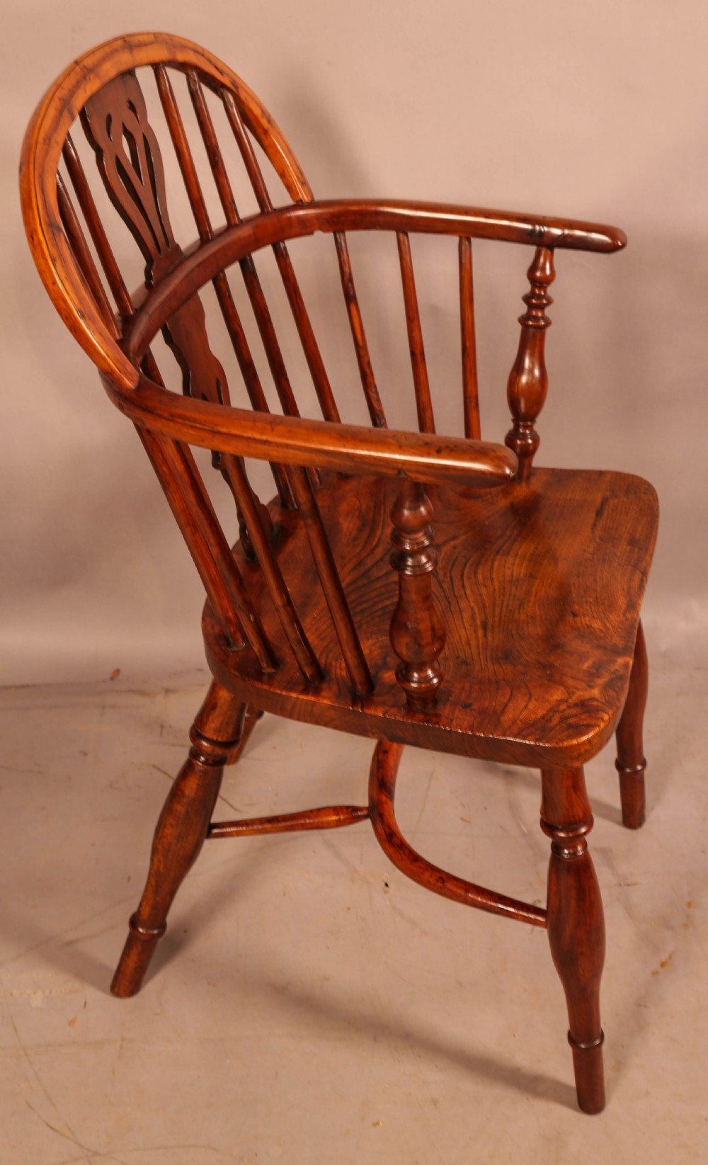 A low back yew wood Windsor armchair featuring turned spindles, a central pierced splat, a shaped seat, and a curved crinoline stretcher.