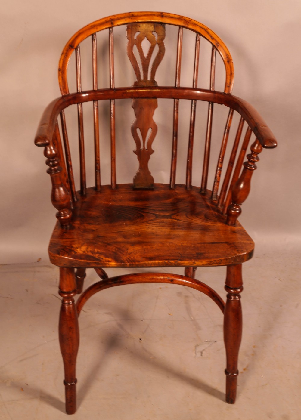 A low back yew wood Windsor armchair featuring turned spindles, a central pierced splat, a shaped seat, and a curved crinoline stretcher. View II