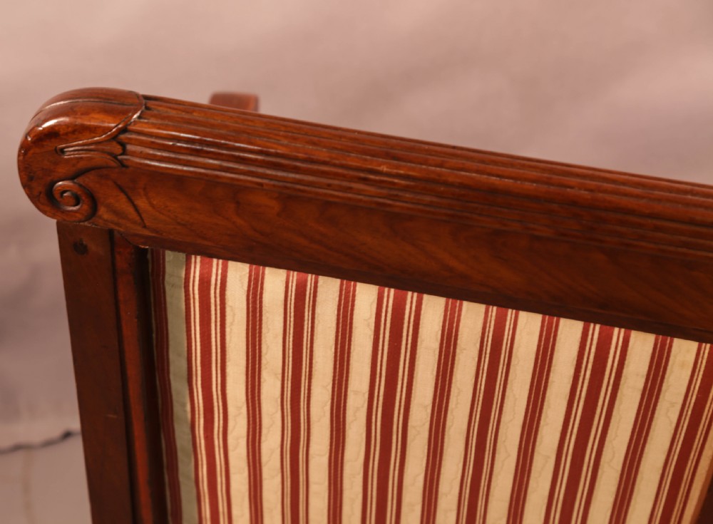 A Regency mahogany settee featuring a striped red and cream upholstered backrest and seat cushion, accented with gilded decorative carvings along the wooden frame. View X