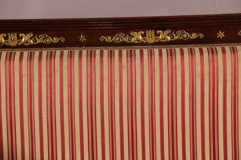 A Regency mahogany settee featuring a striped red and cream upholstered backrest and seat cushion, accented with gilded decorative carvings along the wooden frame. View XV
