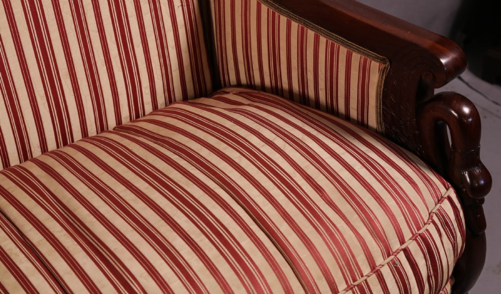 A Regency mahogany settee featuring a striped red and cream upholstered backrest and seat cushion, accented with gilded decorative carvings along the wooden frame. View XVI