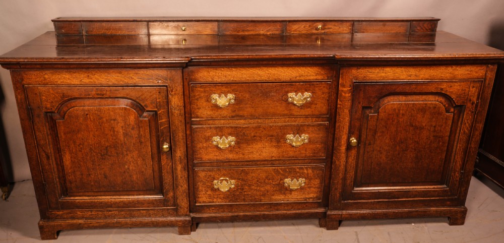 A large antique Georgian oak serving dresser featuring central drawers flanked by panelled cupboards and a stepped top shelf with small drawers.