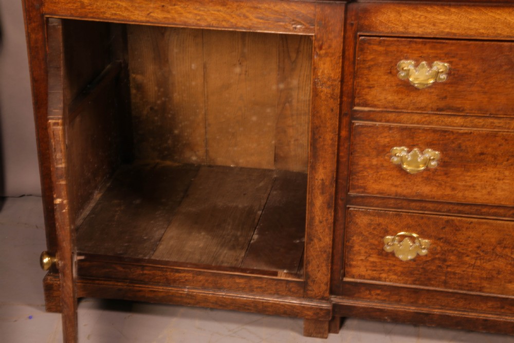 A large antique Georgian oak serving dresser featuring central drawers flanked by panelled cupboards and a stepped top shelf with small drawers. View II