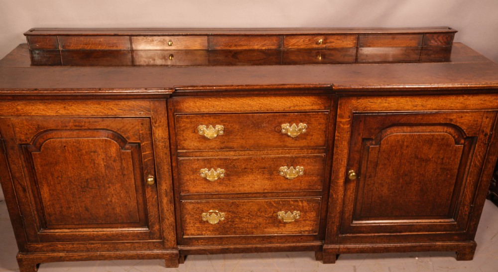 A large antique Georgian oak serving dresser featuring central drawers flanked by panelled cupboards and a stepped top shelf with small drawers. View V