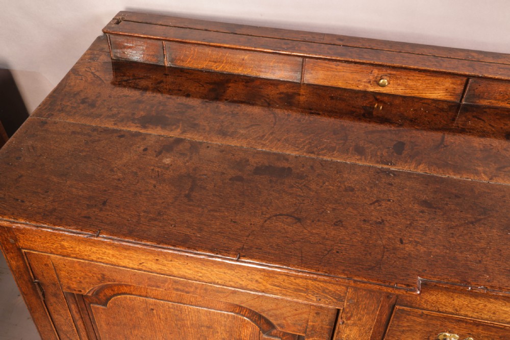 A large antique Georgian oak serving dresser featuring central drawers flanked by panelled cupboards and a stepped top shelf with small drawers. View VI