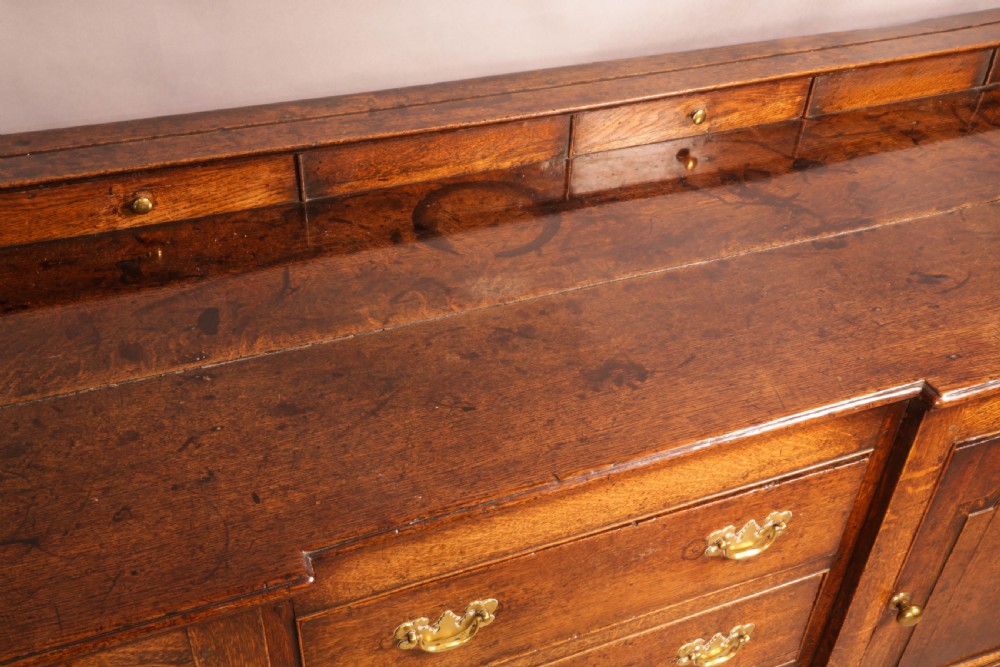 A large antique Georgian oak serving dresser featuring central drawers flanked by panelled cupboards and a stepped top shelf with small drawers. View VII