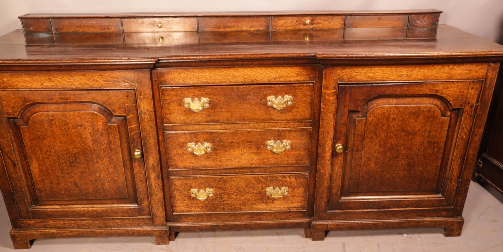 A large antique Georgian oak serving dresser featuring central drawers flanked by panelled cupboards and a stepped top shelf with small drawers. View XII