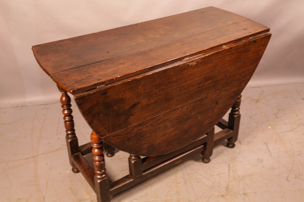 A seventeenth-century oak gateleg dining table featuring two drop leaves, turned legs, perimeter stretchers, and an open end drawer. View II