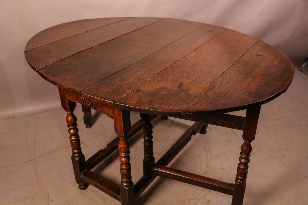A seventeenth-century oak gateleg dining table featuring two drop leaves, turned legs, perimeter stretchers, and an open end drawer. View V