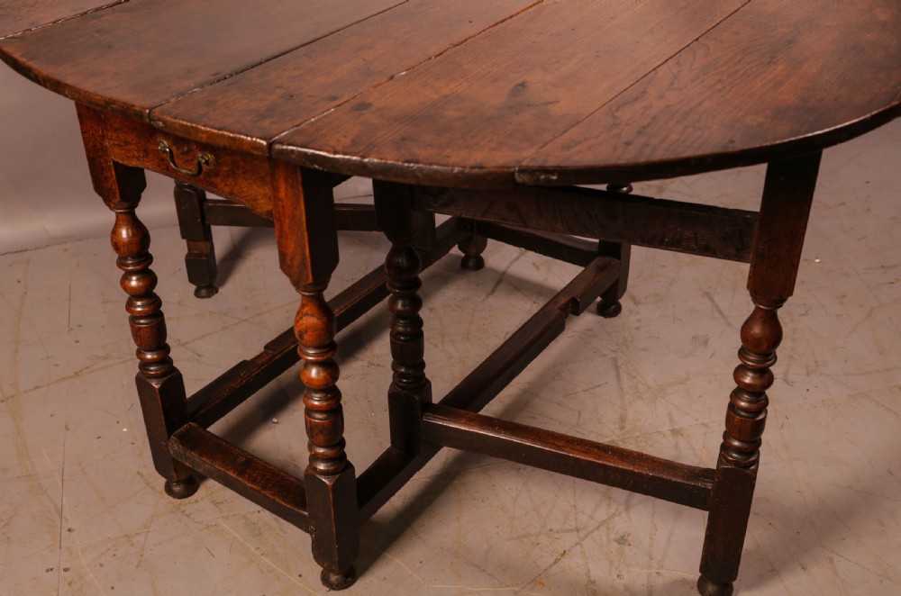 A seventeenth-century oak gateleg dining table featuring two drop leaves, turned legs, perimeter stretchers, and an open end drawer. View VI