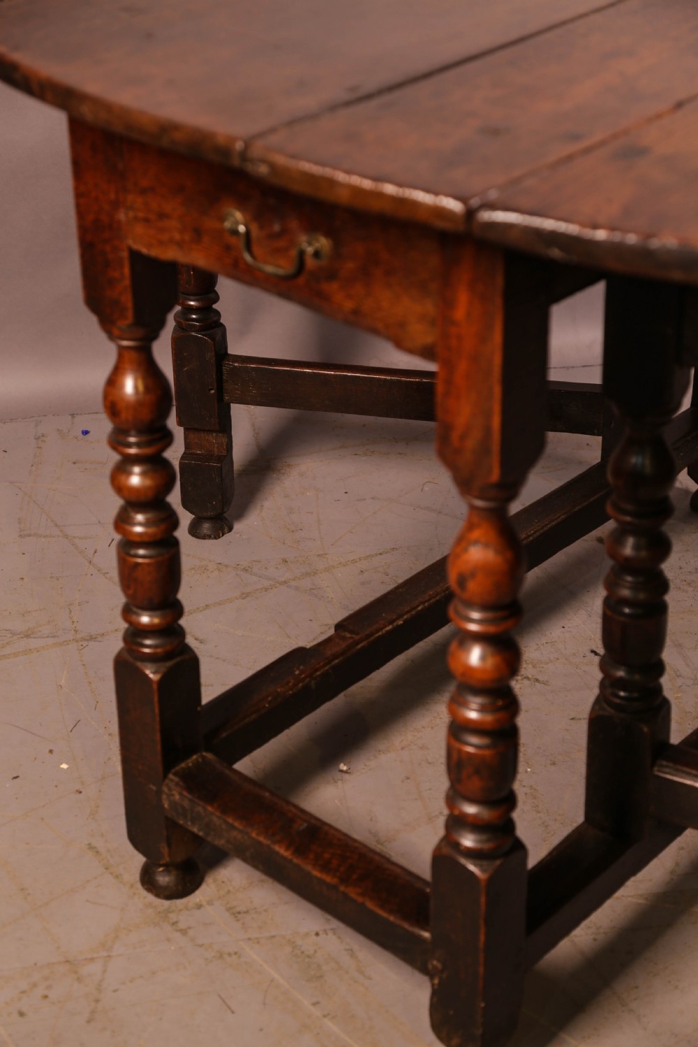 A seventeenth-century oak gateleg dining table featuring two drop leaves, turned legs, perimeter stretchers, and an open end drawer. View VII