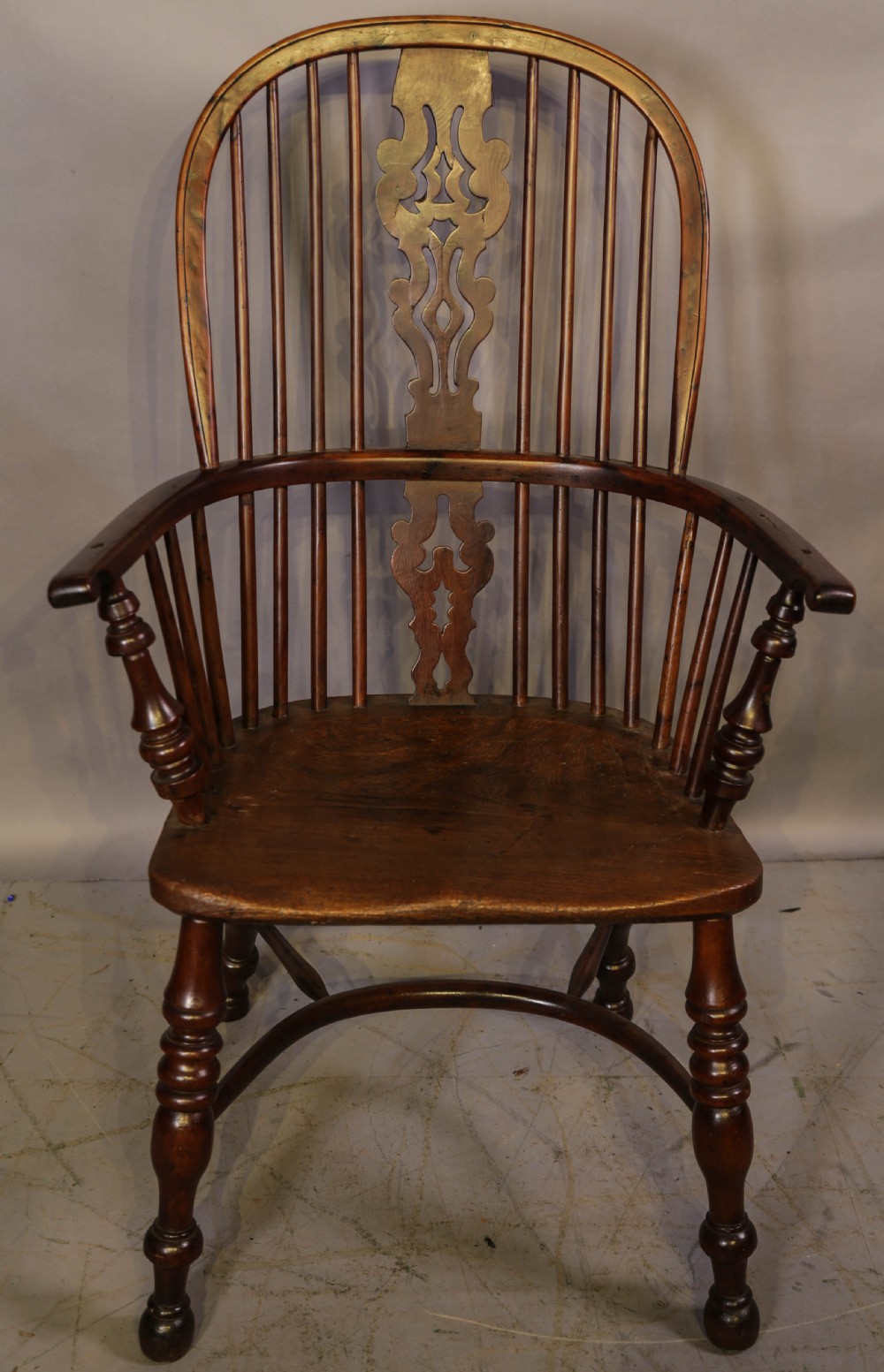A high-back wooden Windsor armchair featuring a bentwood hoop, pierced central splat, turned spindles, sculpted seat, and baluster legs connected by a stretcher.