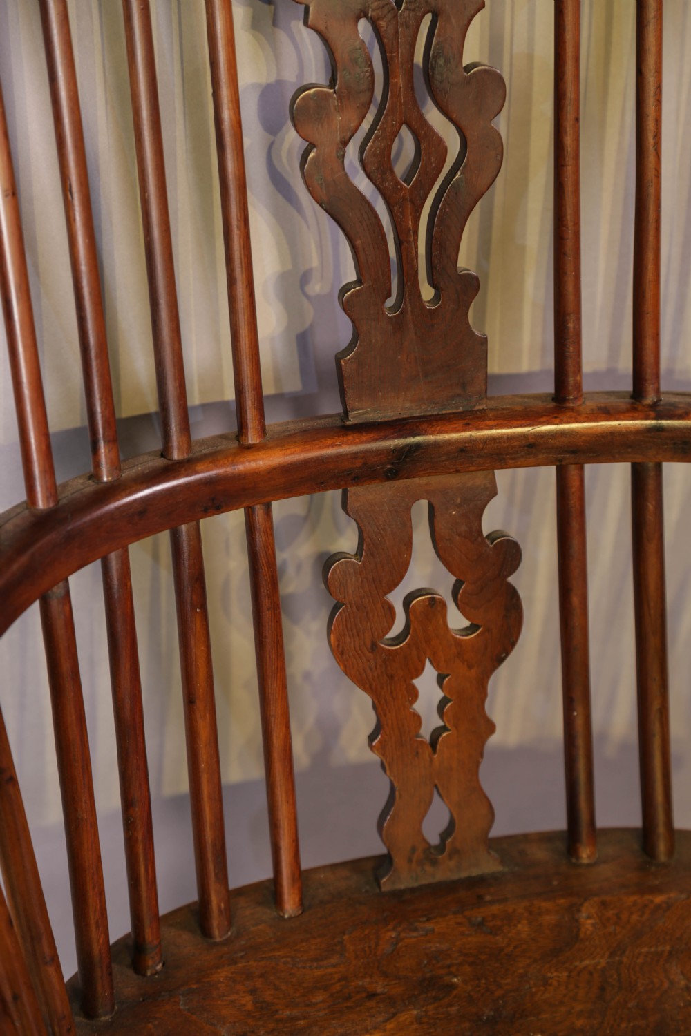 A high-back wooden Windsor armchair featuring a bentwood hoop, pierced central splat, turned spindles, sculpted seat, and baluster legs connected by a stretcher. View X