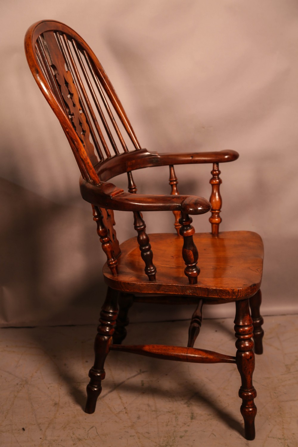 A 19th-century yew wood Windsor armchair featuring a curved hoop back, central pierced splat, turned spindles, broad armrests, and turned legs.