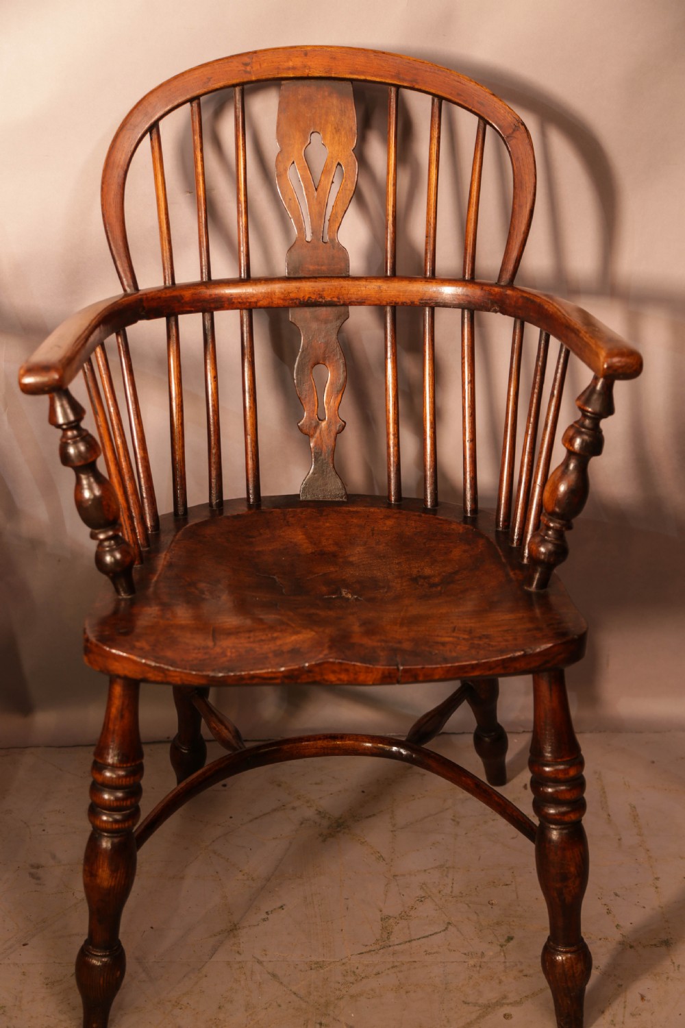 Two antique wooden armchairs featuring curved backrests, central pierced splats, spindle supports, and solid saddle seats. View V