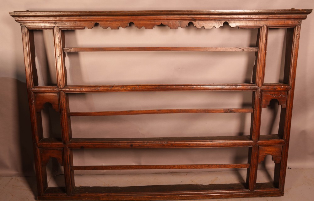 A Georgian dark oak plate rack featuring a scalloped top frieze, horizontal retaining bars, and side alcoves with shaped arch cutouts.