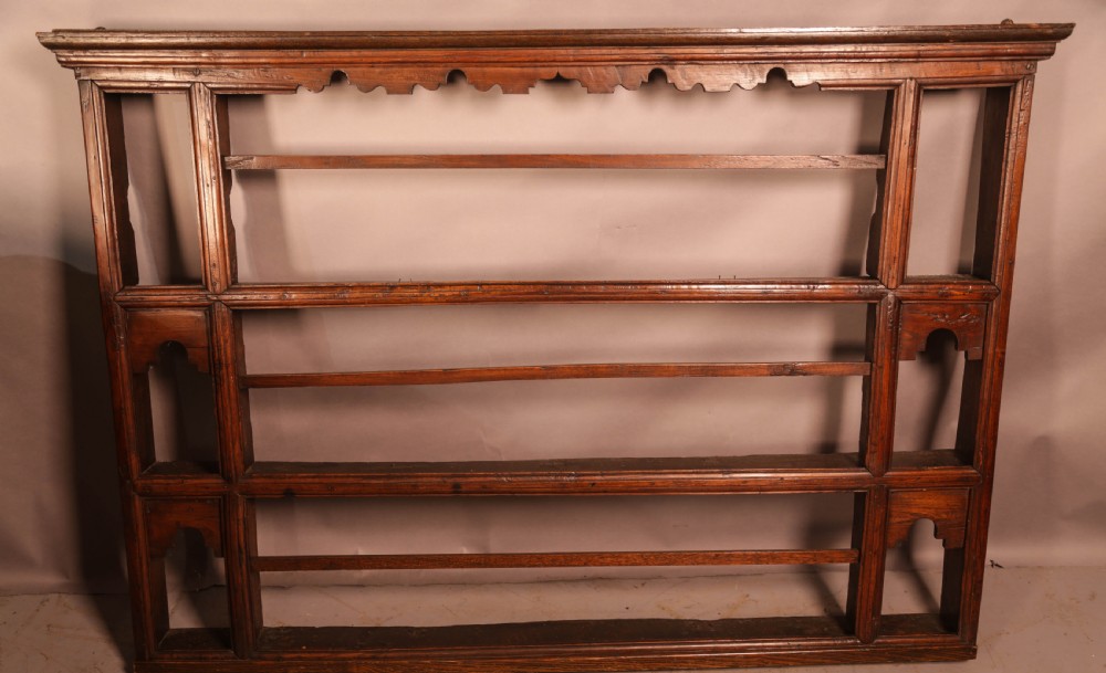 A Georgian dark oak plate rack featuring a scalloped top frieze, horizontal retaining bars, and side alcoves with shaped arch cutouts. View II