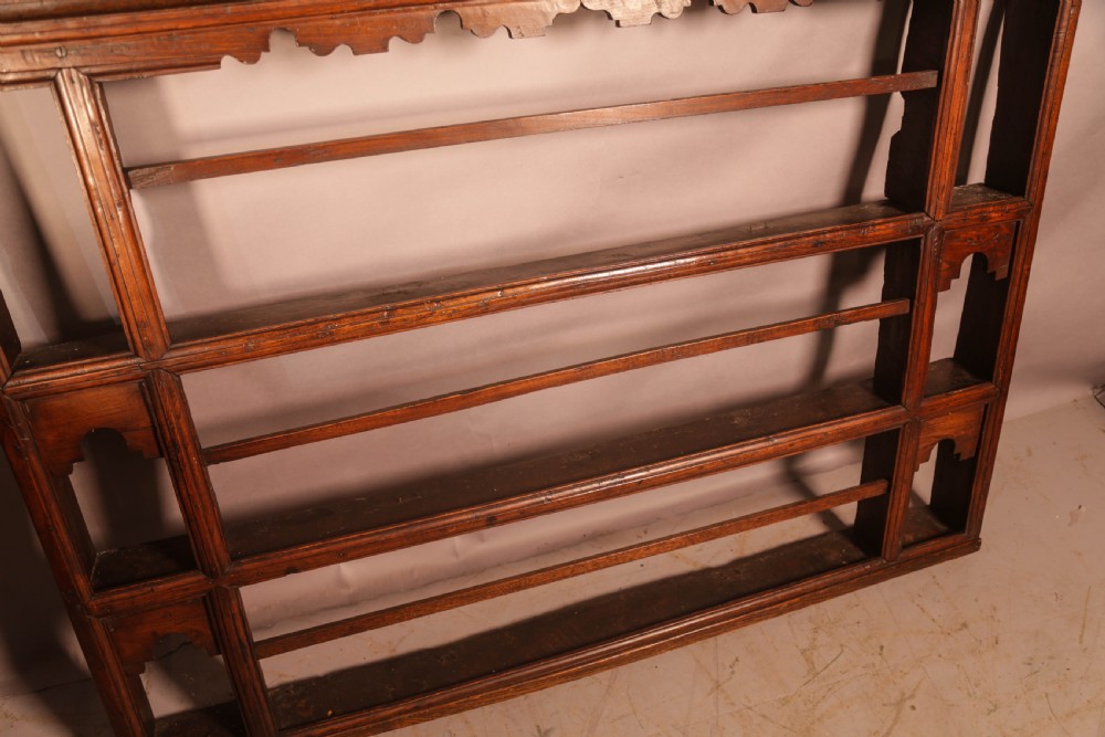 A Georgian dark oak plate rack featuring a scalloped top frieze, horizontal retaining bars, and side alcoves with shaped arch cutouts. View IX