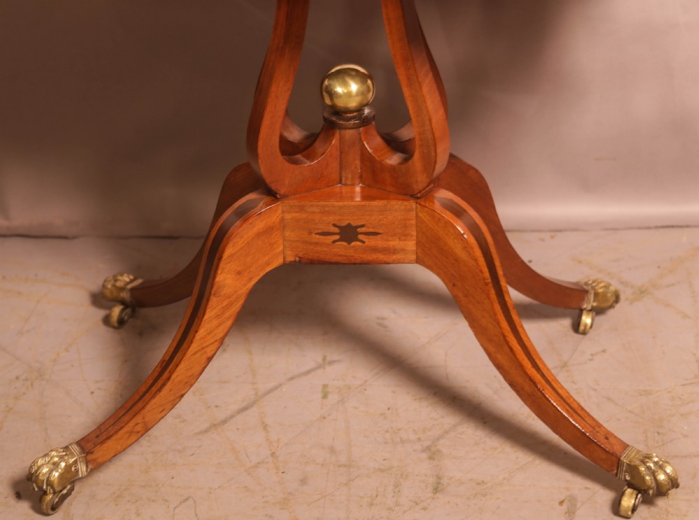An antique Regency mahogany fold-over games table with a curved frieze, central pedestal support, and splayed legs with brass paw feet. View III