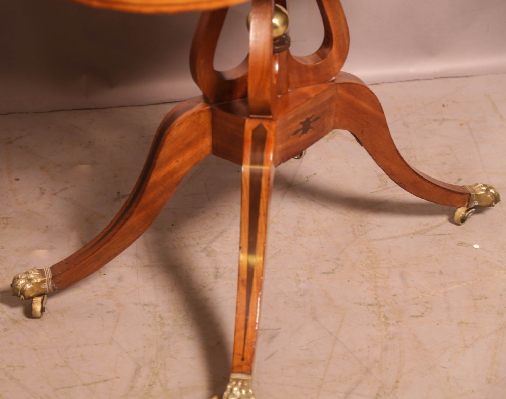 An antique Regency mahogany fold-over games table with a curved frieze, central pedestal support, and splayed legs with brass paw feet. View V