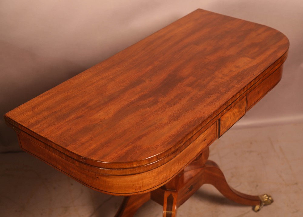 An antique Regency mahogany fold-over games table with a curved frieze, central pedestal support, and splayed legs with brass paw feet. View VI